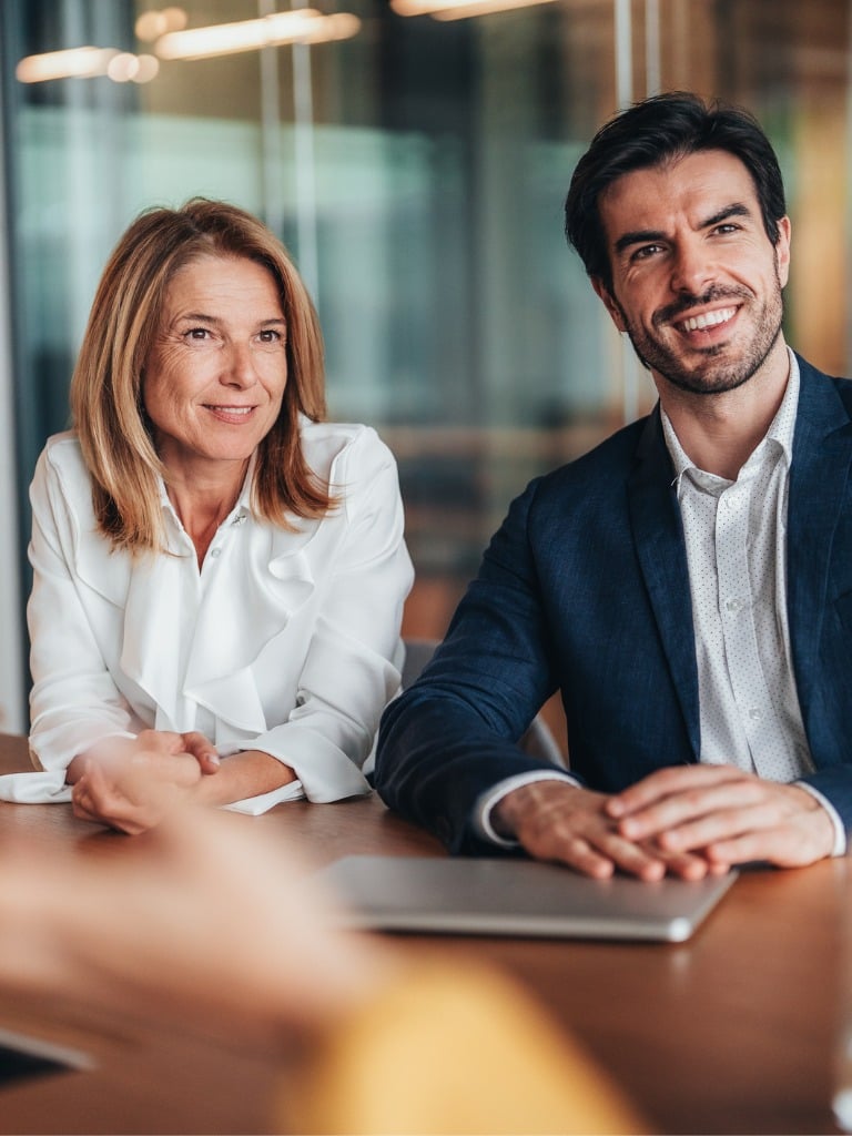 Business meeting with a man and woman smiling and sitting at a table with a laptop.
