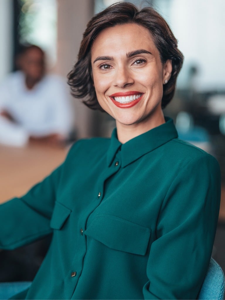 Smiling businesswoman in a teal blouse with short brown hair and red lipstick.